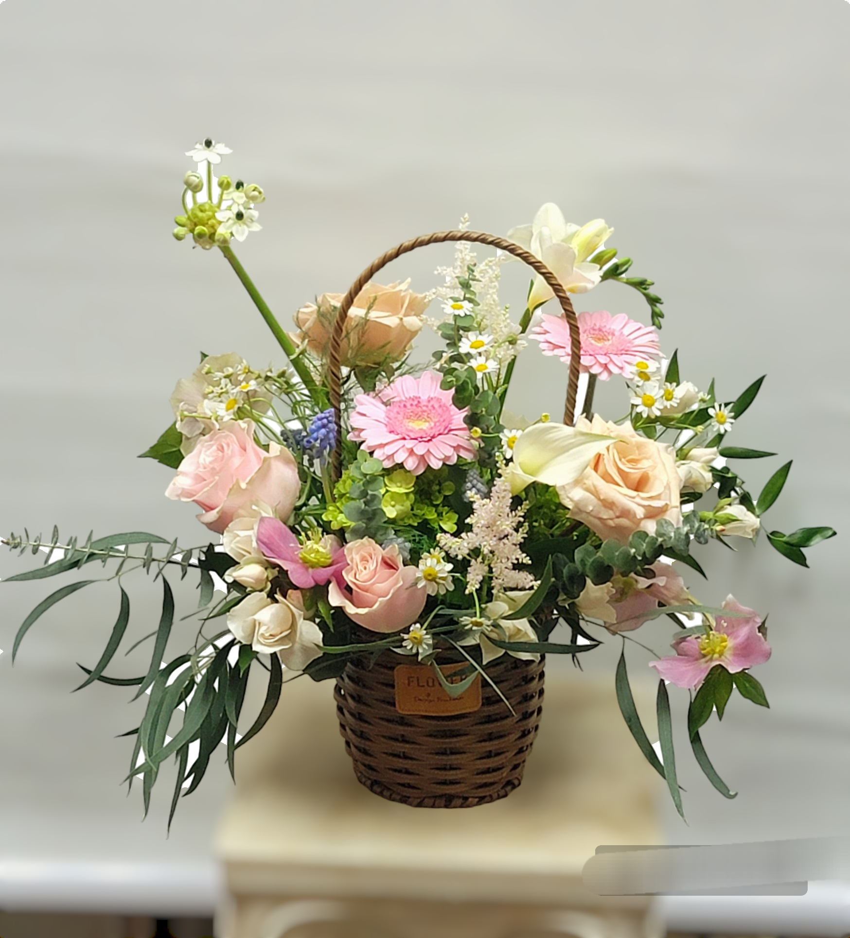 Basket arrangement of pink and peach flowers with a woven handle