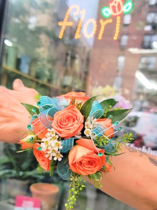 Small coral rose wrist corsage with blue ribbon and white filler flowers
