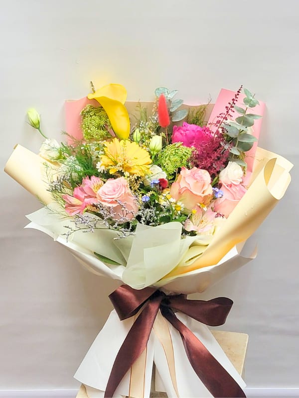 Mixed bouquet with pink and yellow flowers wrapped in cream paper