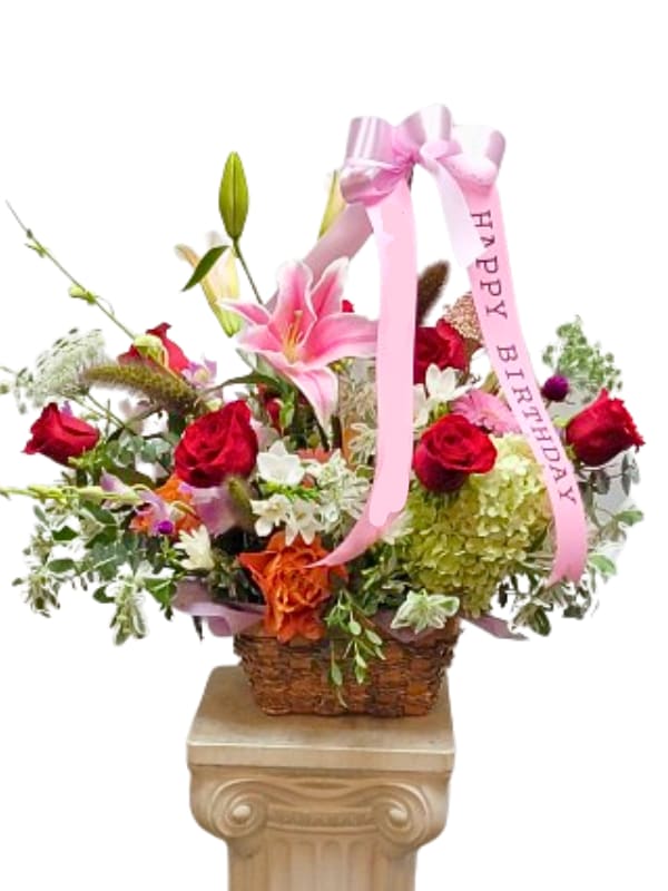 Basket arrangement with pink lilies, red roses, and a pink birthday ribbon