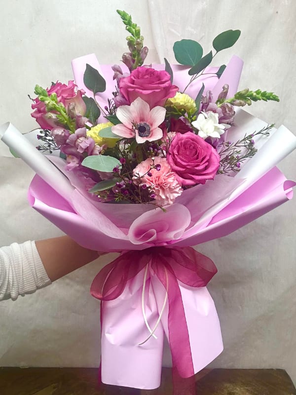 Pink rose bouquet with mixed blooms wrapped in pink paper and ribbon