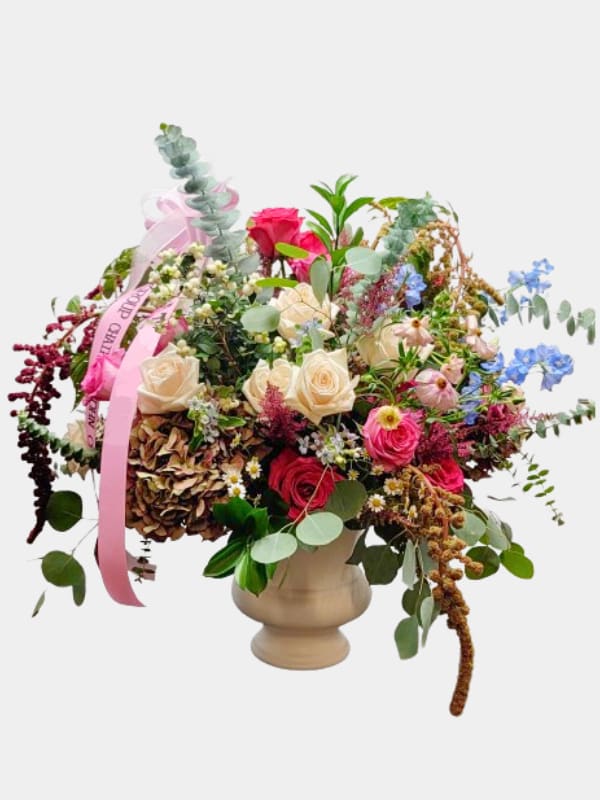 Mixed bouquet of roses and wildflowers in a beige vase with pink ribbon