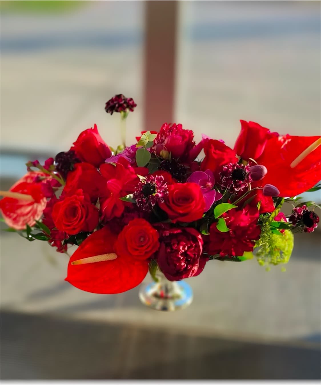 Winter Wishes Centerpiece - This striking red-themed flower centerpiece is the perfect addition to elevate any special occasion. Featuring a luxurious blend of vibrant, high-end blooms, it effortlessly enhances the beauty of your event. With its rich colors and elegant arrangement, this centerpiece will bring sophistication and charm, creating a memorable atmosphere for your celebration. Let the exquisite harmony of these flowers transform your day into something truly unforgettable.