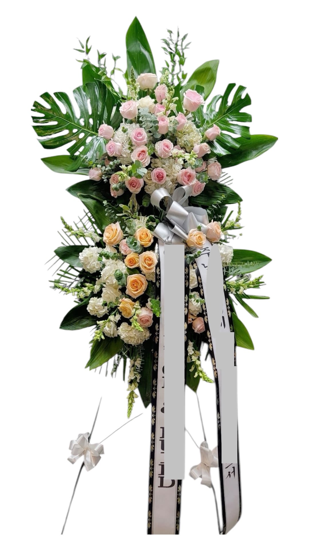 Tall standing floral spray with pink and peach roses and large tropical leaves