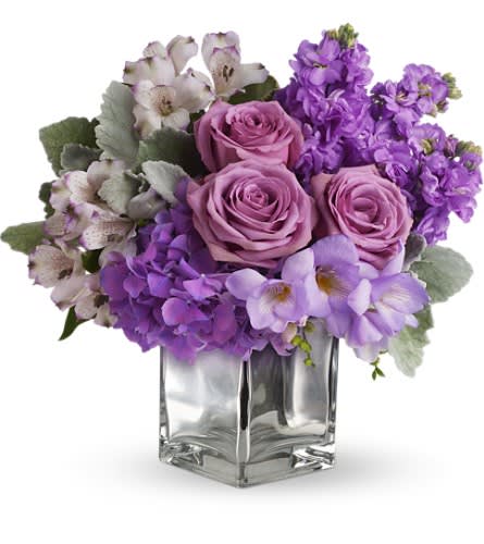 Purple roses and mixed lavender flowers in a clear glass vase