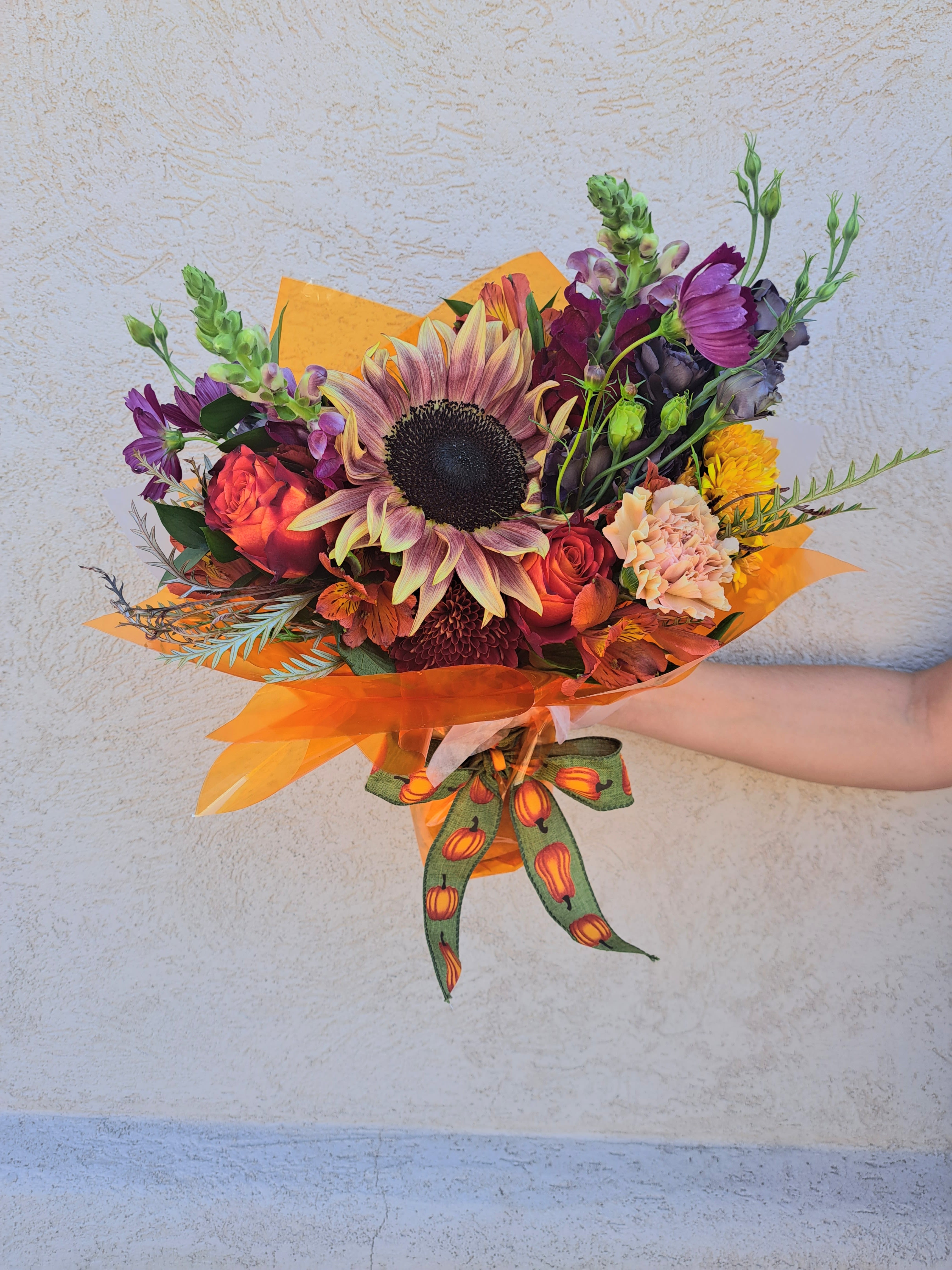 Mixed bouquet with a large sunflower and orange-purple blooms wrapped in orange paper