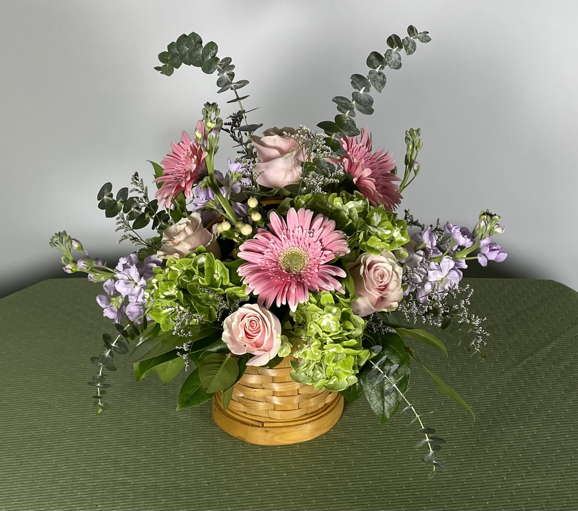 Pink gerbera daisies and roses in a woven basket with lavender accents