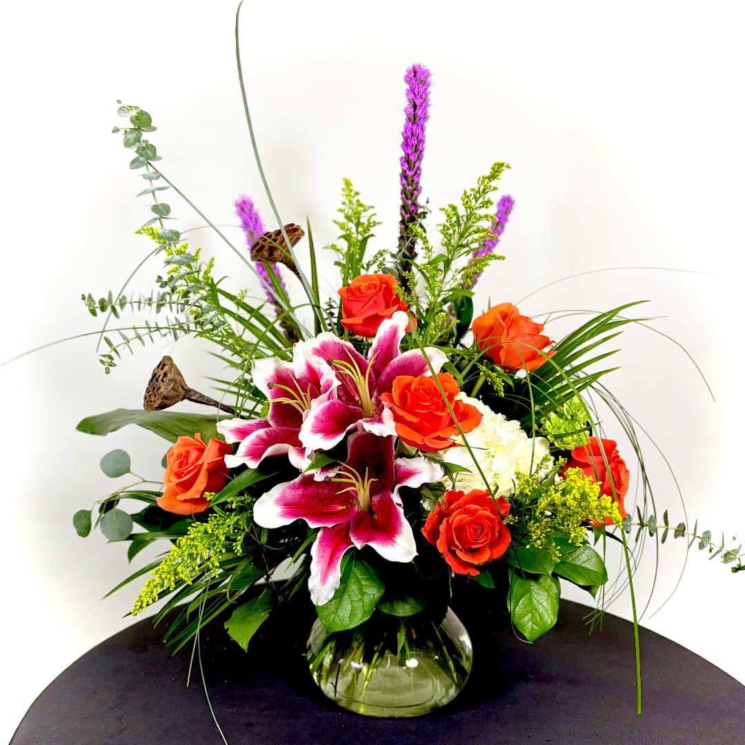 Orange roses and pink lilies in a glass vase with tall greenery