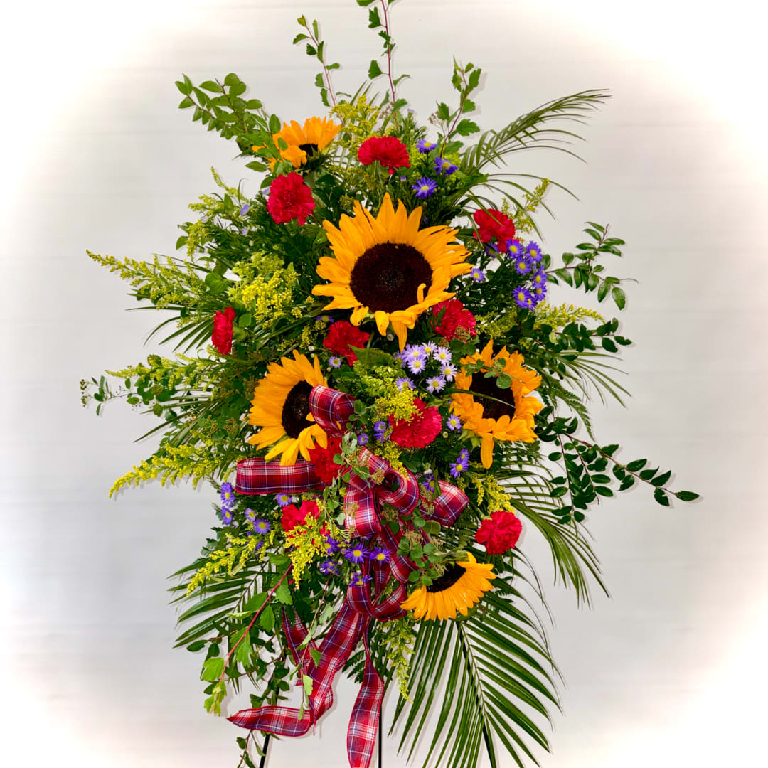 Tall floral spray with sunflowers, red carnations, purple daisies, and plaid ribbon