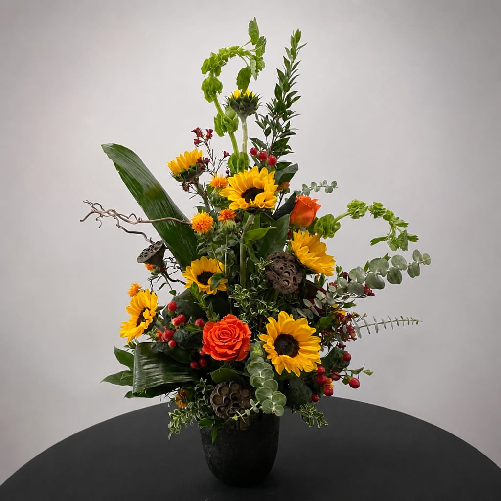Tall mixed floral arrangement with sunflowers and orange roses in a black vase