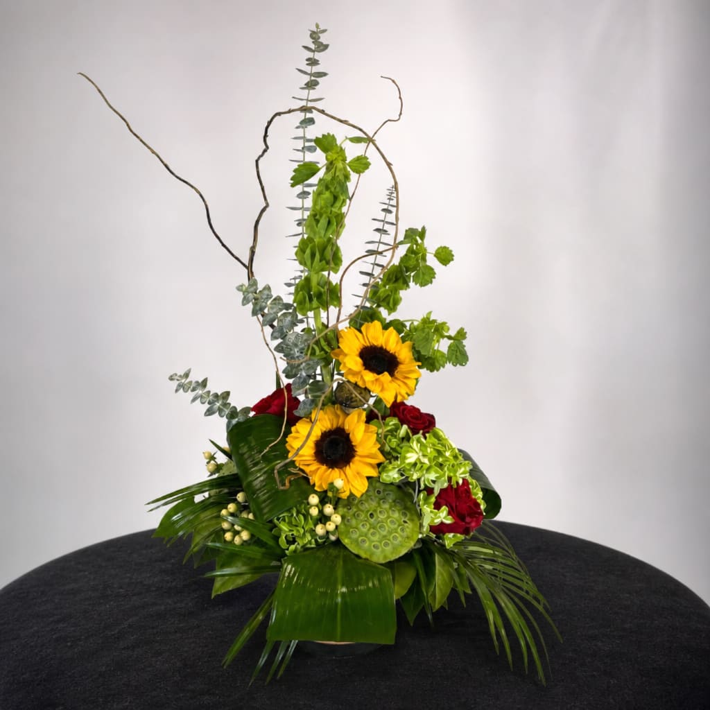 Tall floral arrangement with sunflowers and red roses in a low container