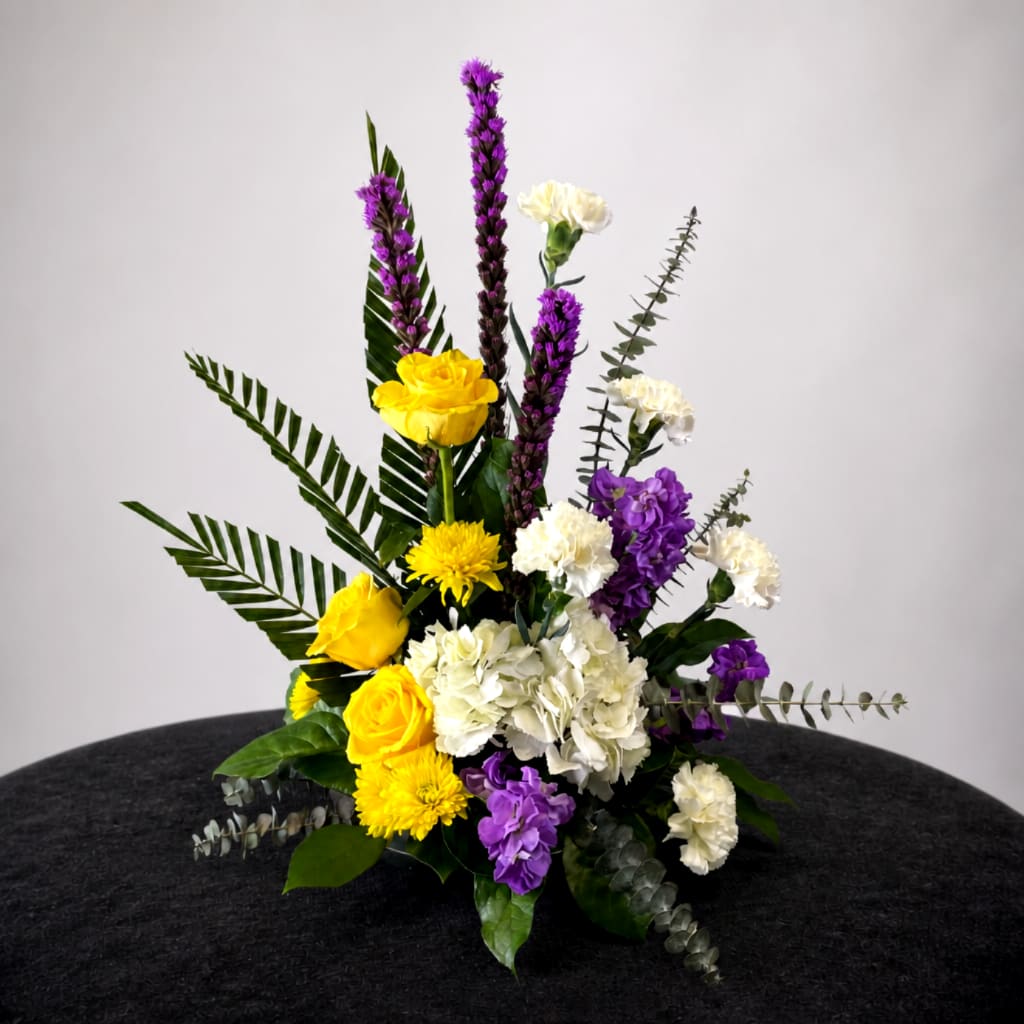 Yellow, white, and purple floral arrangement in a low container