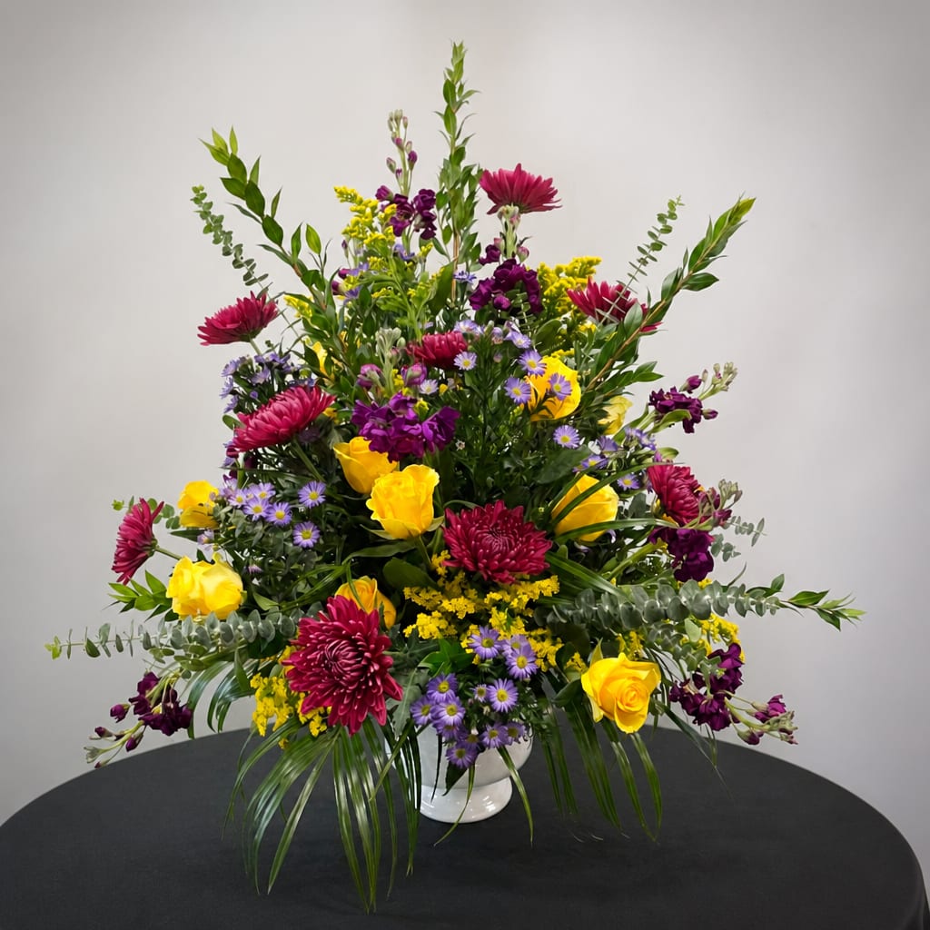 Mixed bouquet of yellow roses, purple blooms, and magenta flowers in a white vase