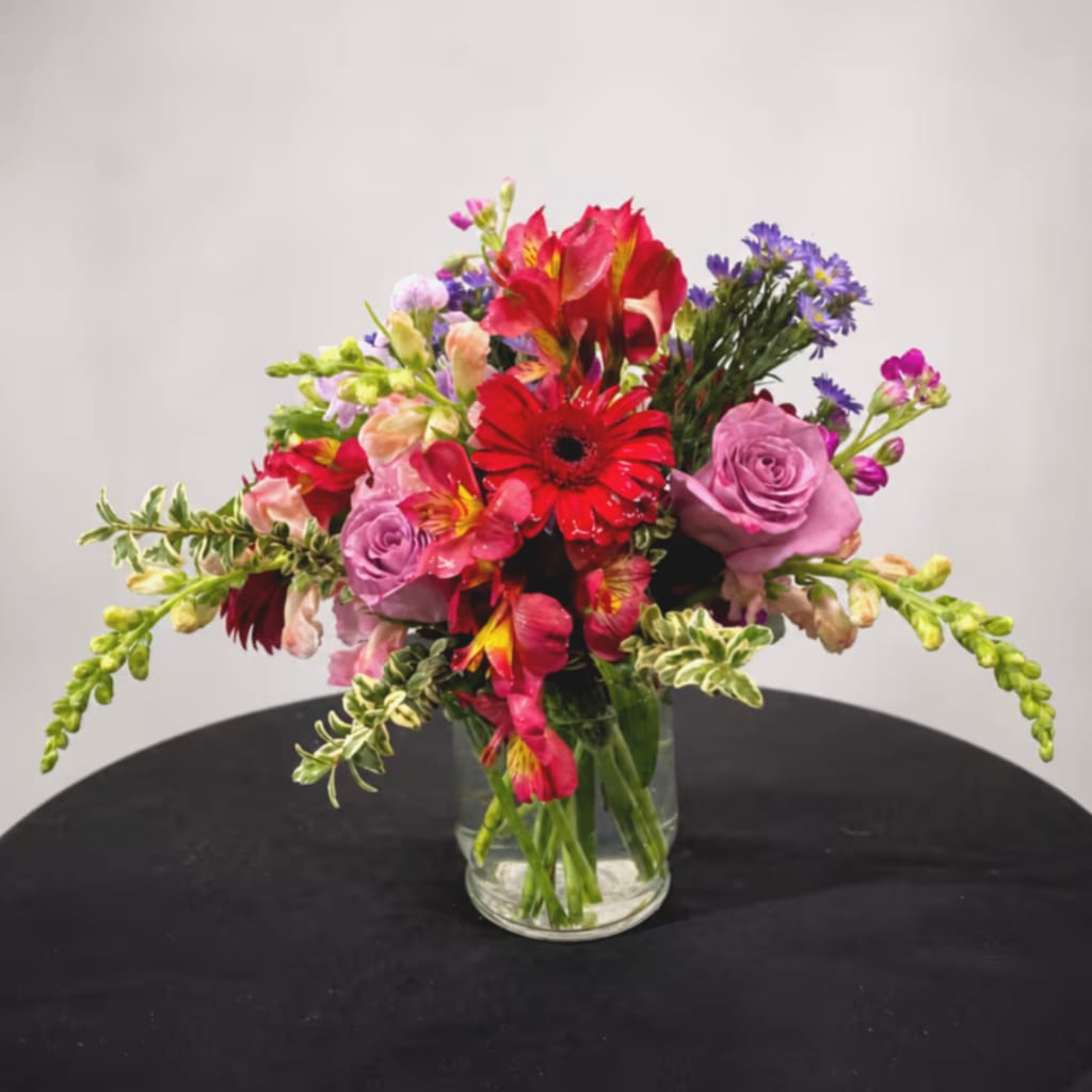 Mixed bouquet of red, pink, and purple flowers in a clear glass vase