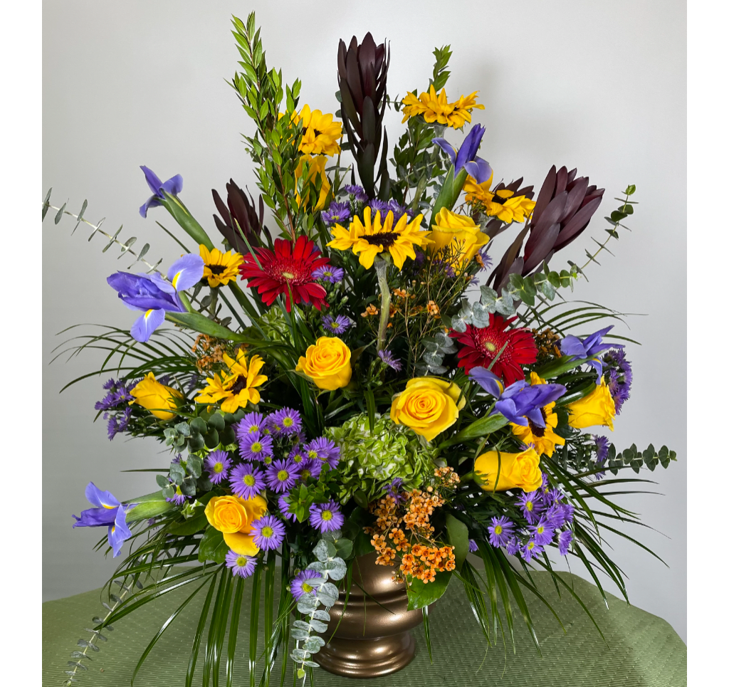 Colorful mixed bouquet in a bronze vase with yellow, purple, red, and dark blooms