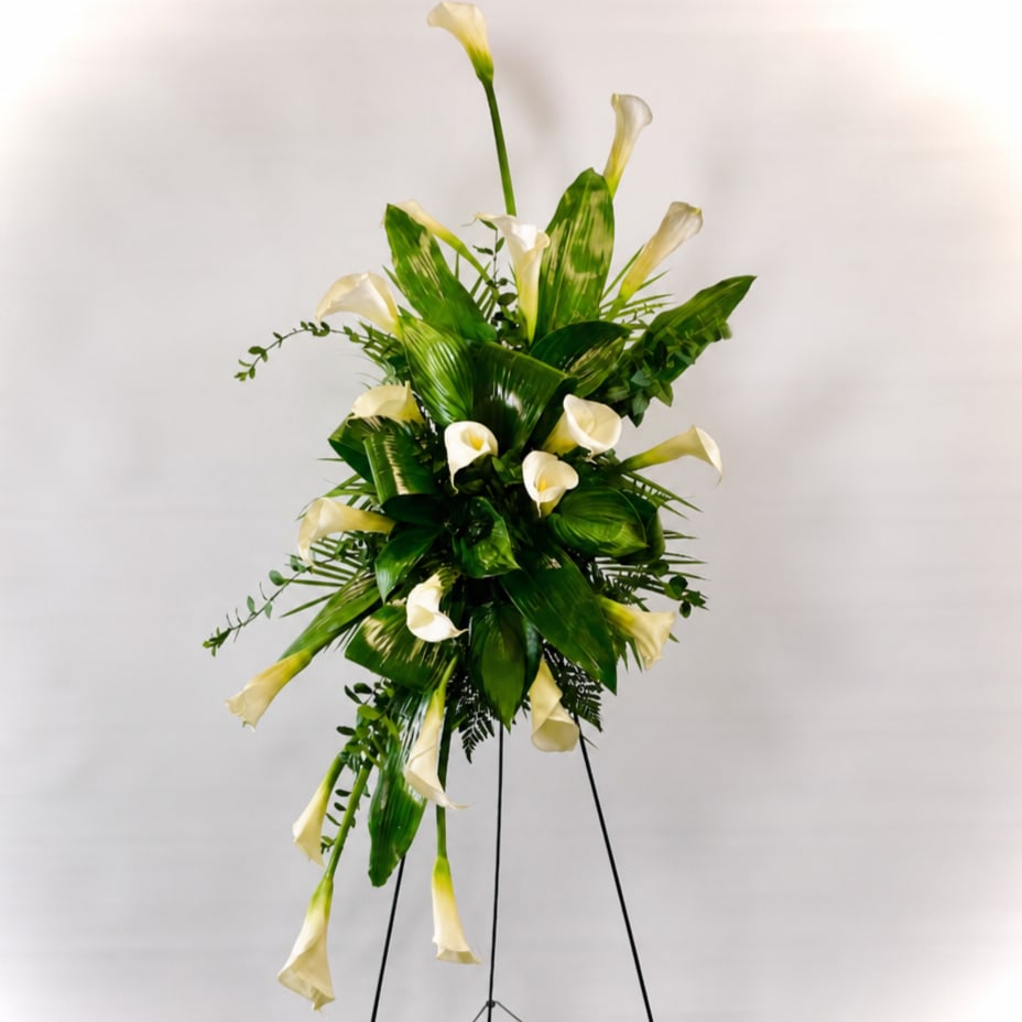 Tall standing arrangement of white calla lilies and green foliage on a black easel