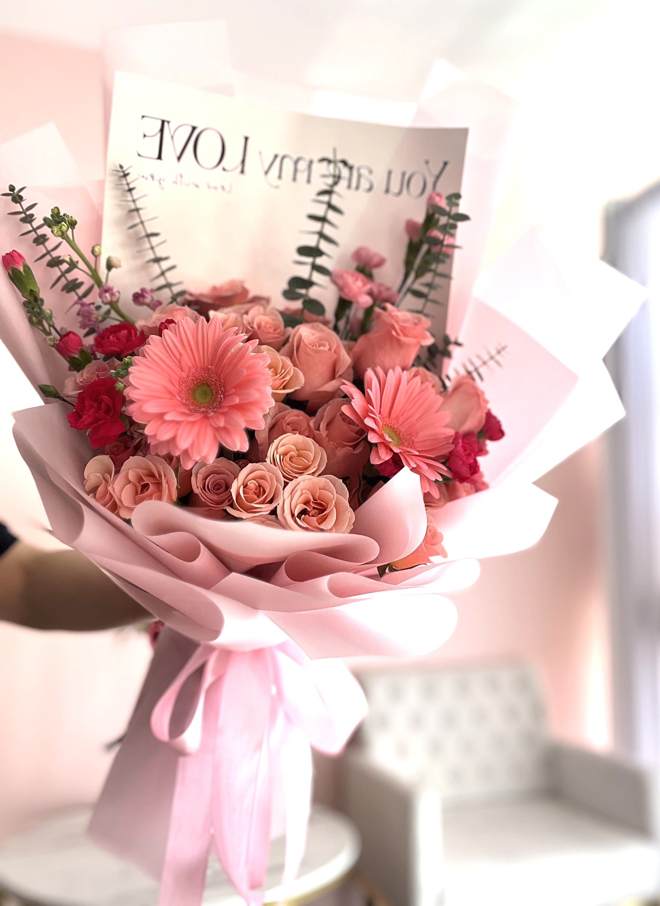 Pink bouquet of roses and gerbera daisies wrapped in pastel paper