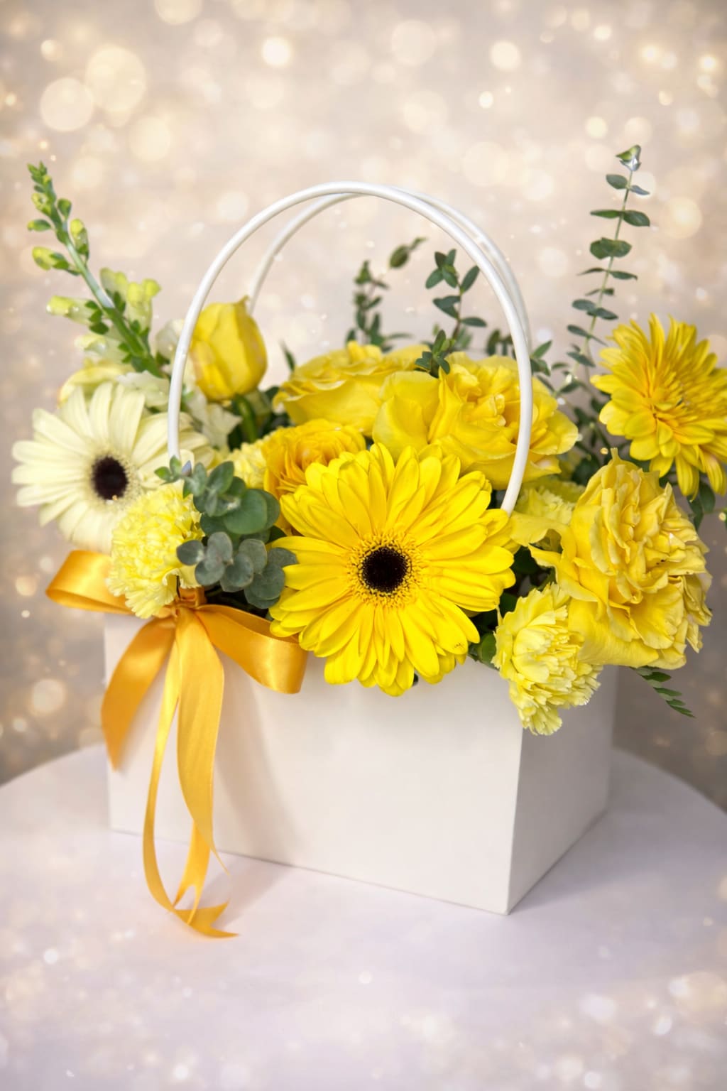 Yellow and white flower arrangement in a white handled box with a yellow ribbon bow.