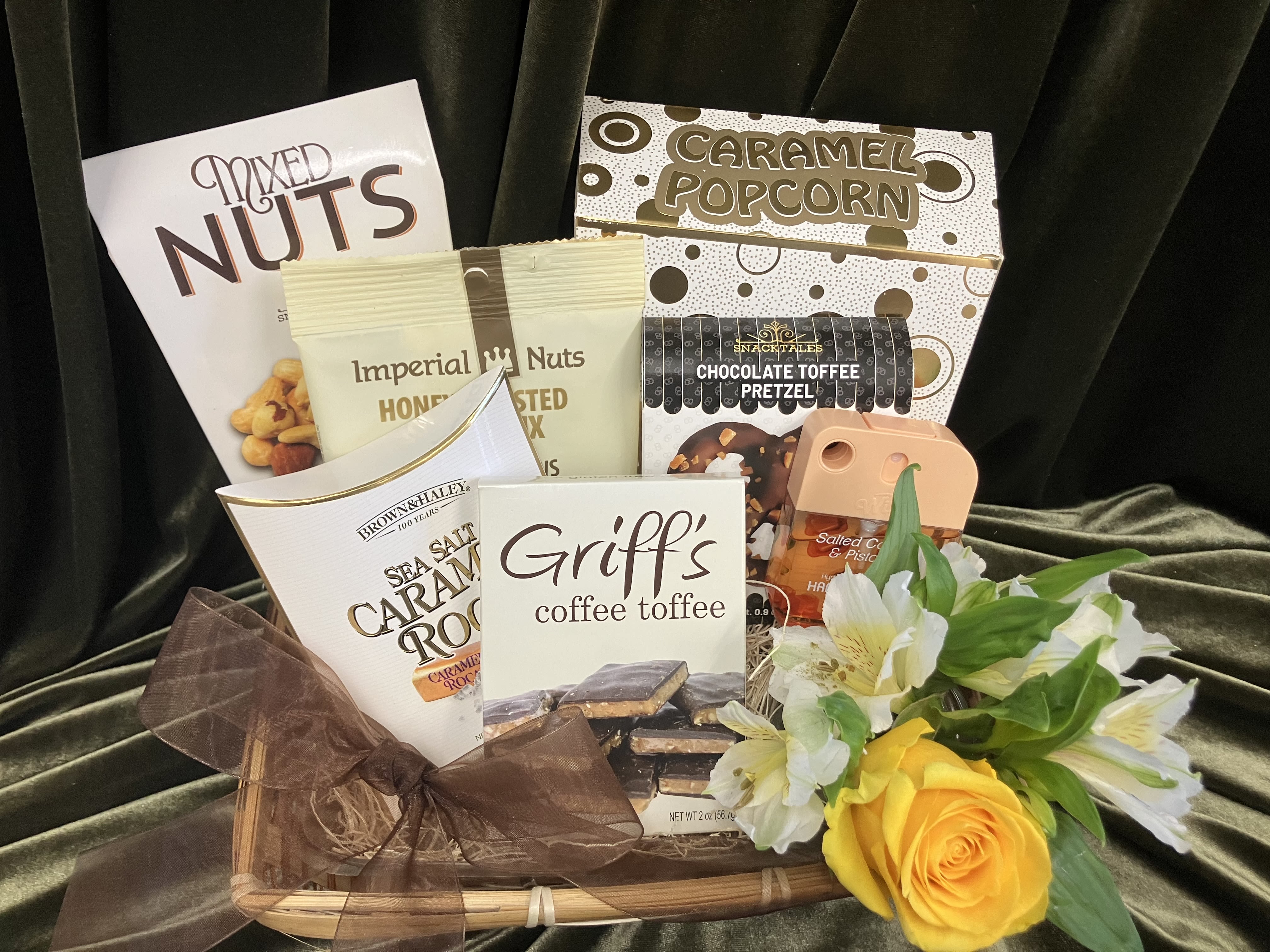 Sweet Tooth Snack Basket - Sweet goodies are arranged in a woven basket with a sheer brown ribbon for a ready-to-give presentation. The floral accent sits at the front-one yellow rose and sprays of white alstroemeria add some cheer bringing visual warmth and natural texture to the snacks. Ideal for coworkers, neighbors, or friends who love treats, it arrives wrapped and ready to delight the person you're thinking of.