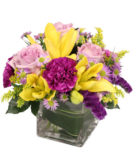 Mixed bouquet of yellow lilies, pink roses, and purple flowers in a glass vase
