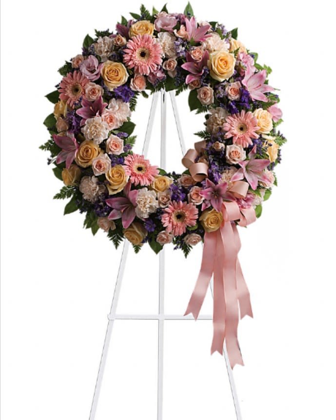 Floral wreath on a white stand with pink and yellow blooms and a pink ribbon