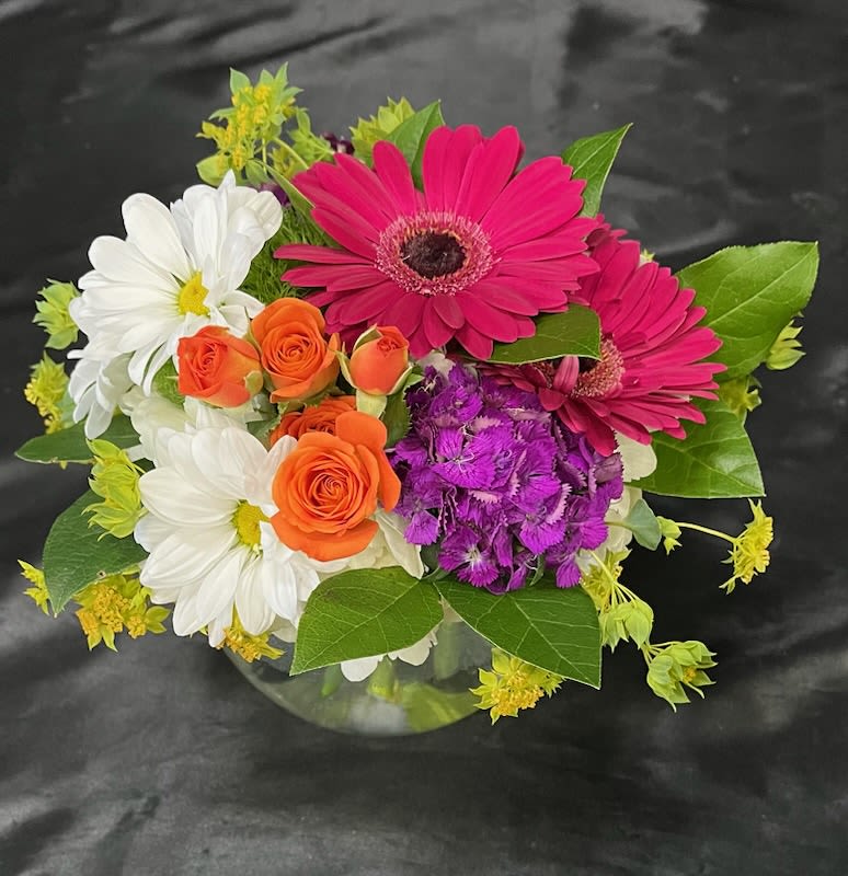 Bouquet of pink gerbera daisies, white daisies, and orange roses in a glass vase