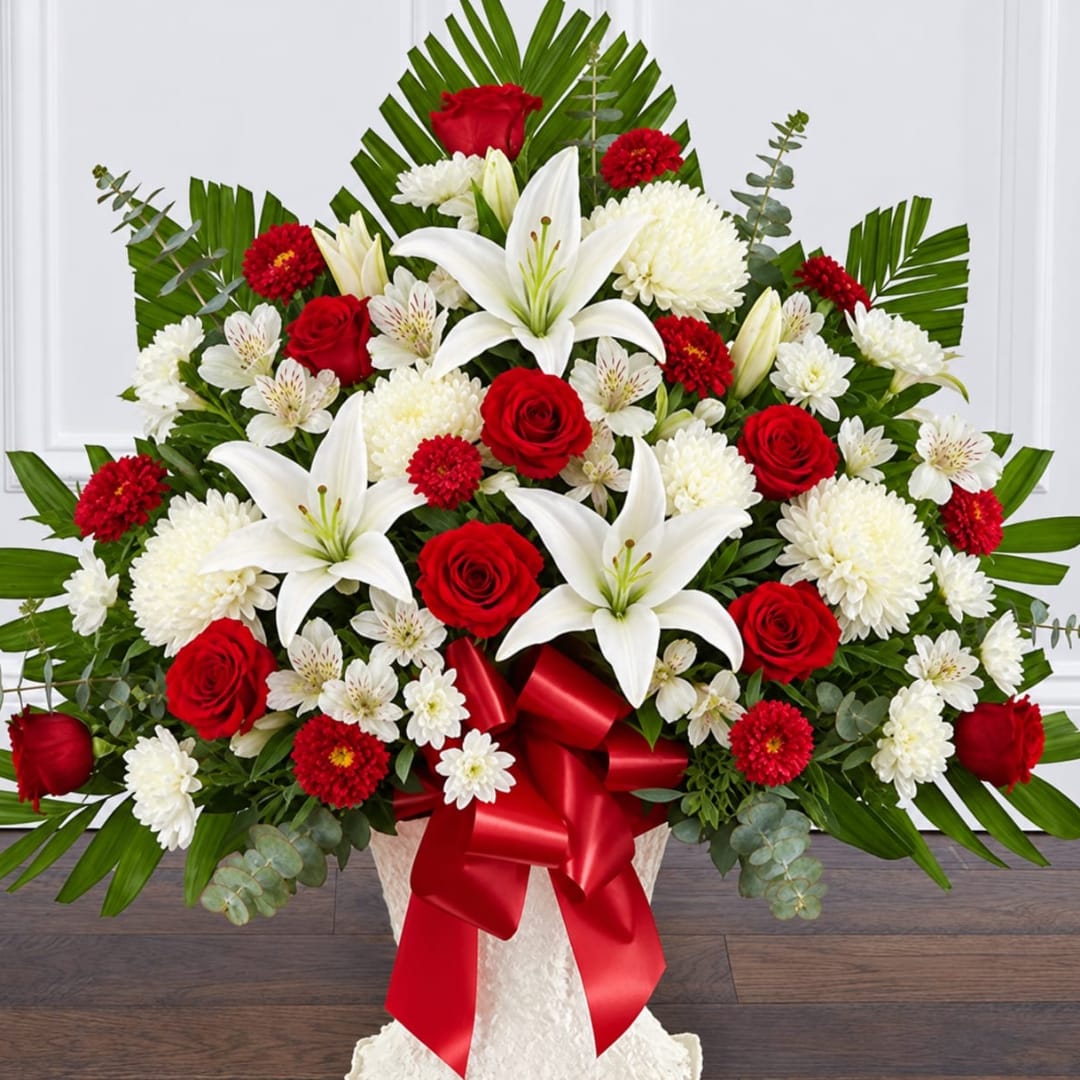Large red, white, and green floral arrangement with lilies and roses in a white vase