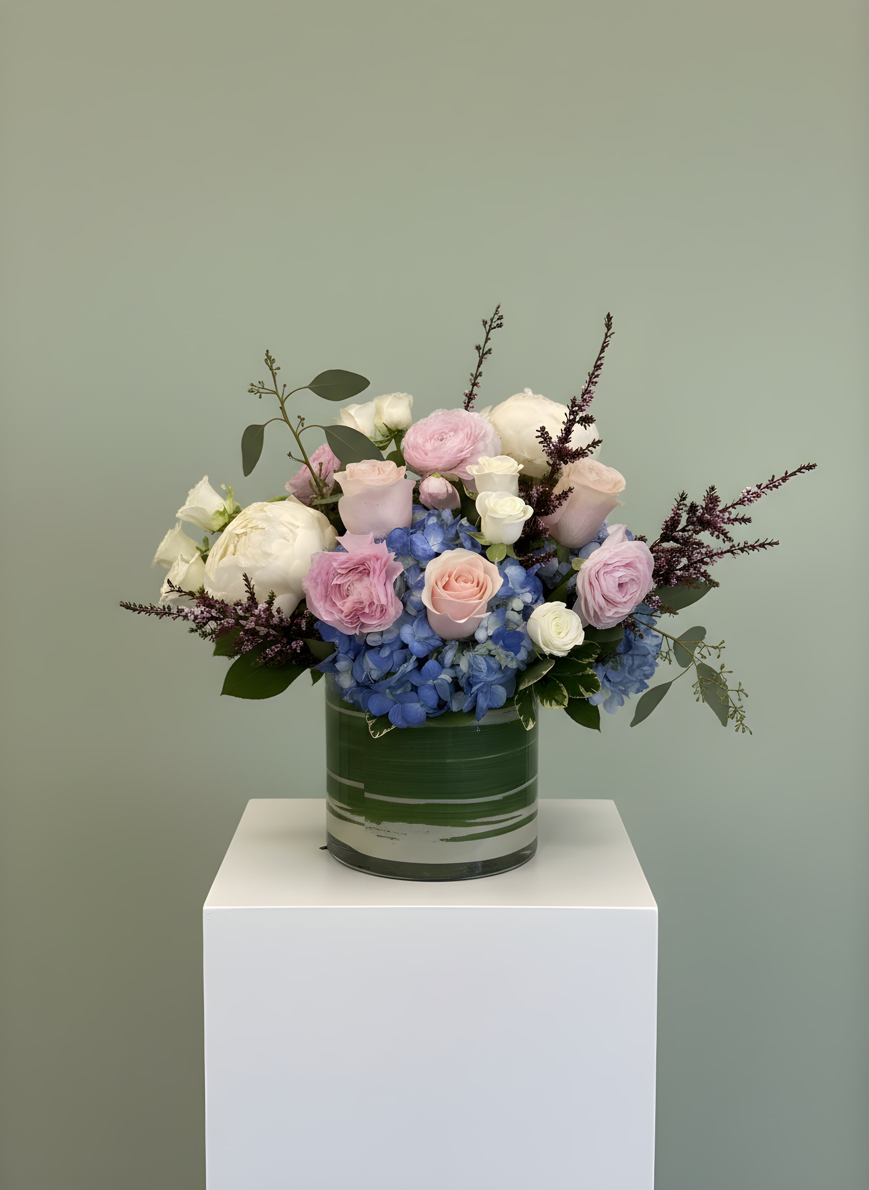 Lunelle - Lunelle is an elegant and romantic floral arrangement featuring lush blue hydrangeas, soft blush roses, white roses, peonies, and fresh eucalyptus arranged in a modern green glass cylinder vase. Designed with premium fresh flowers, this luxurious arrangement offers a timeless garden-inspired look perfect for birthdays, anniversaries, sympathy occasions, congratulations, or simply brightening someone's day.  Handcrafted by All Occasions Florist in Dallas, Texas, Lunelle combines soft pastel colors with seasonal blooms to create a sophisticated design that complements any home or office. The blend of blue hydrangeas, blush pink roses, creamy white flowers, and textured accents creates a fresh and graceful presentation suitable for both modern and classic styles.  Whether you're celebrating a special occasion or sending a thoughtful gift, Lunelle makes a beautiful statement. Available for same-day flower delivery in Dallas, Highland Park, University Park, Uptown, Oak Lawn, Preston Hollow, and surrounding communities, this premium arrangement is carefully designed to deliver beauty and lasting impressions.  Order Lunelle online today from All Occasions Florist for fresh flower delivery in Dallas and experience the beauty of handcrafted floral arrangements created with exceptional quality and attention to detail.