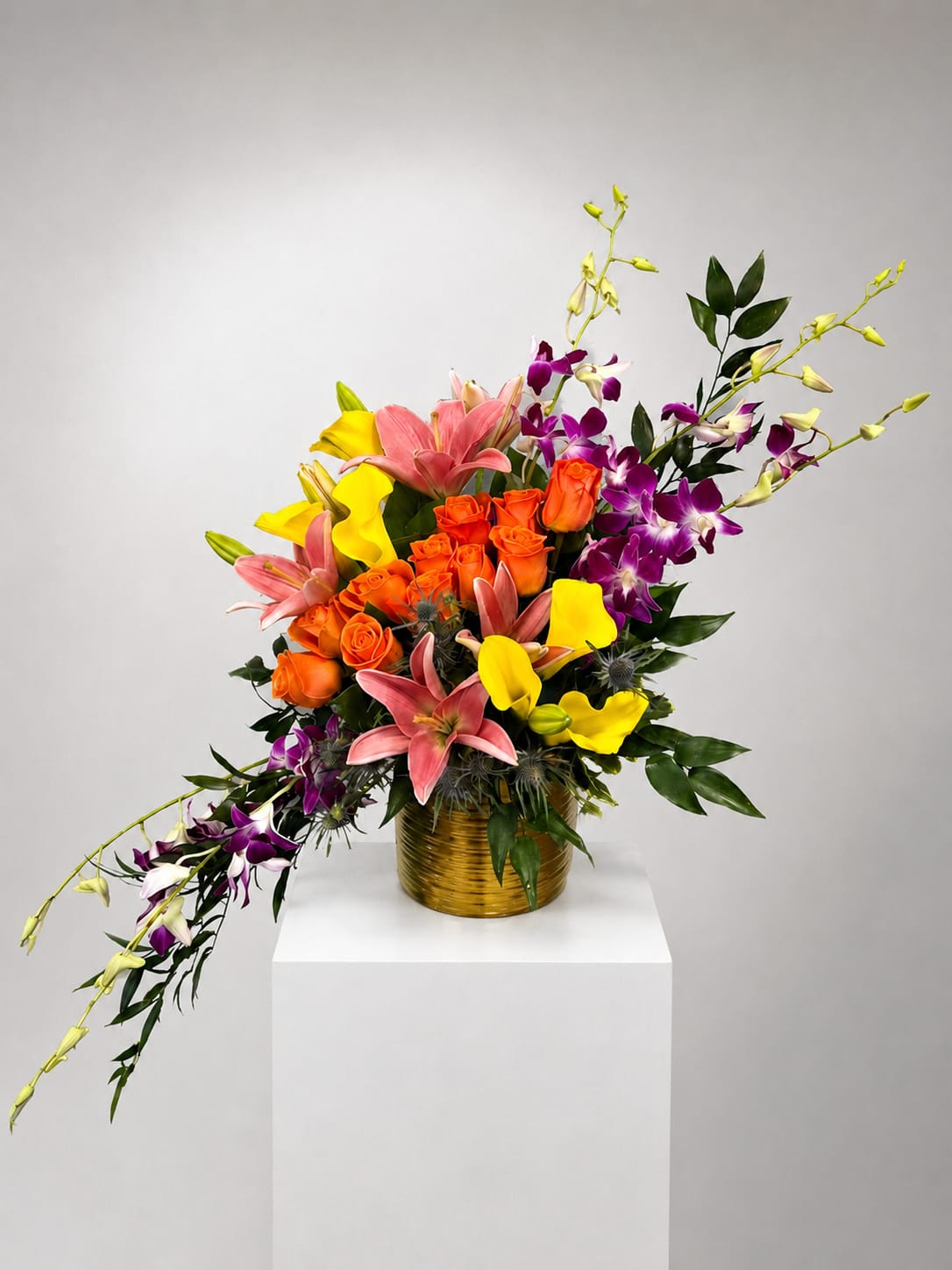 Colorful bouquet of roses, lilies, and orchids in a gold vase