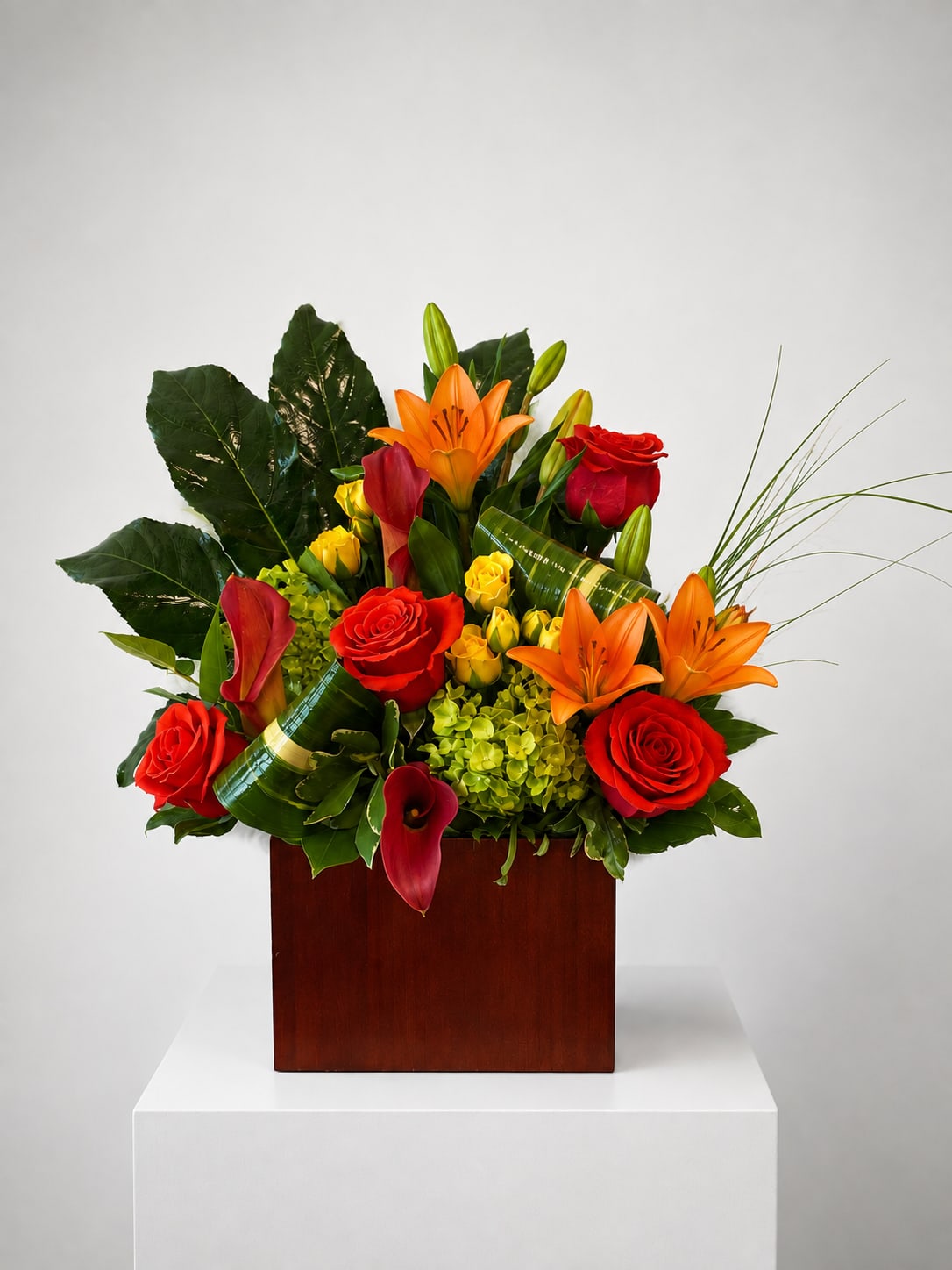 Tropical arrangement with red roses, orange lilies, and calla lilies in a wooden box
