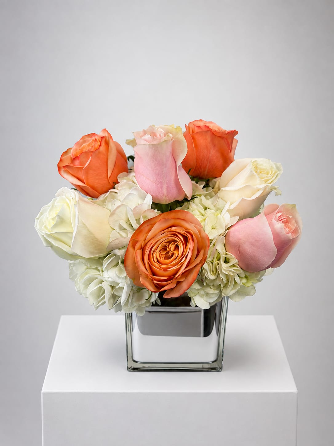 Bouquet of orange, pink, and white roses in a square glass vase