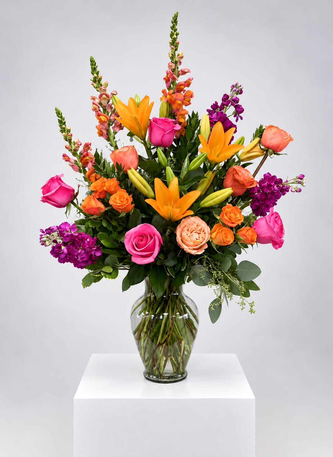 Bright mixed bouquet with roses, lilies, and purple blooms in a glass vase