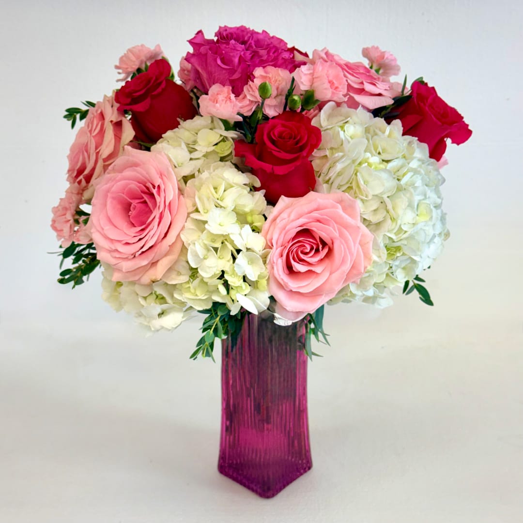Pink and red roses with white hydrangeas in a tall magenta vase