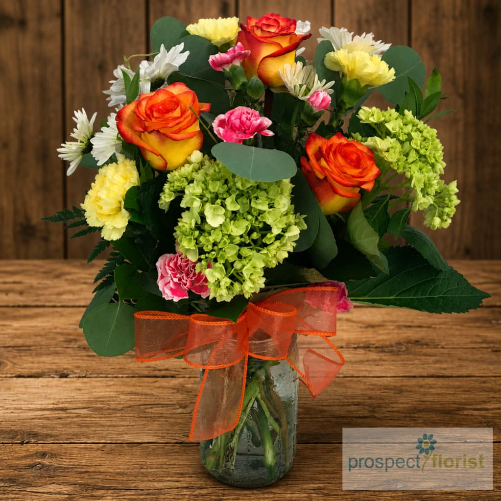 Mixed bouquet of orange roses, hydrangeas, carnations, and daisies in a glass vase