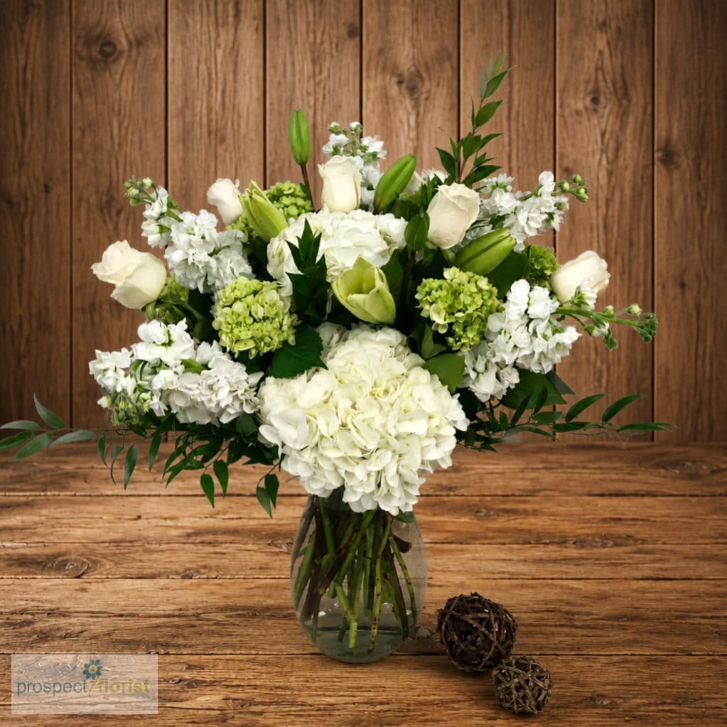 White floral arrangement in a glass vase with green accents
