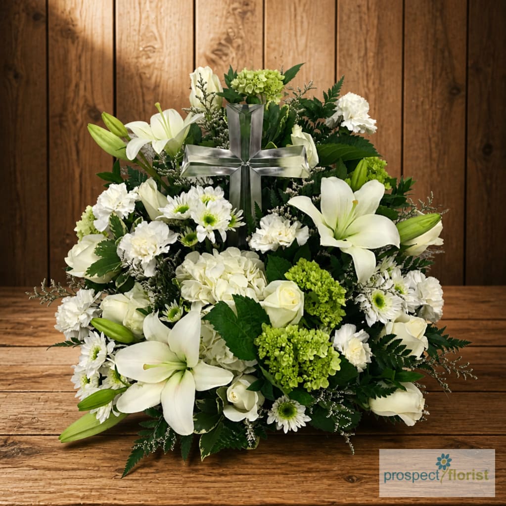 White floral arrangement with lilies, roses, and a silver cross centerpiece