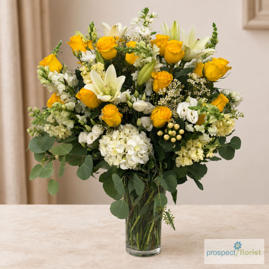 Yellow roses and white lilies arranged in a clear glass vase