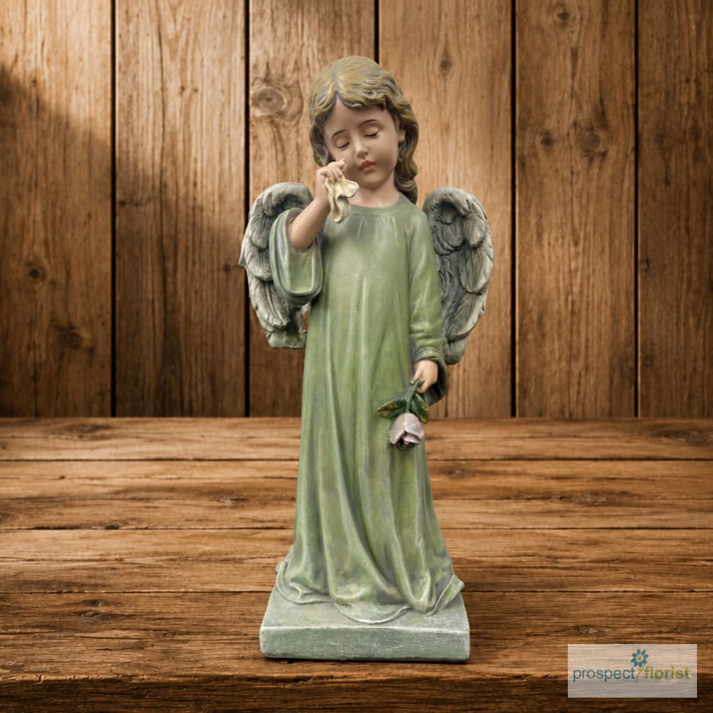 Angel figurine in a green robe holding a flower on a wooden background