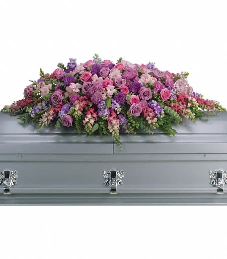Long pink and purple mixed flower casket spray arranged on top of a gray casket