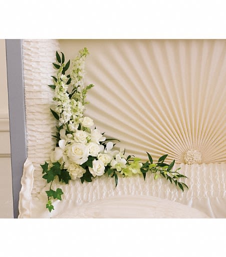 White floral corner spray with roses and other blooms inside a cream casket interior