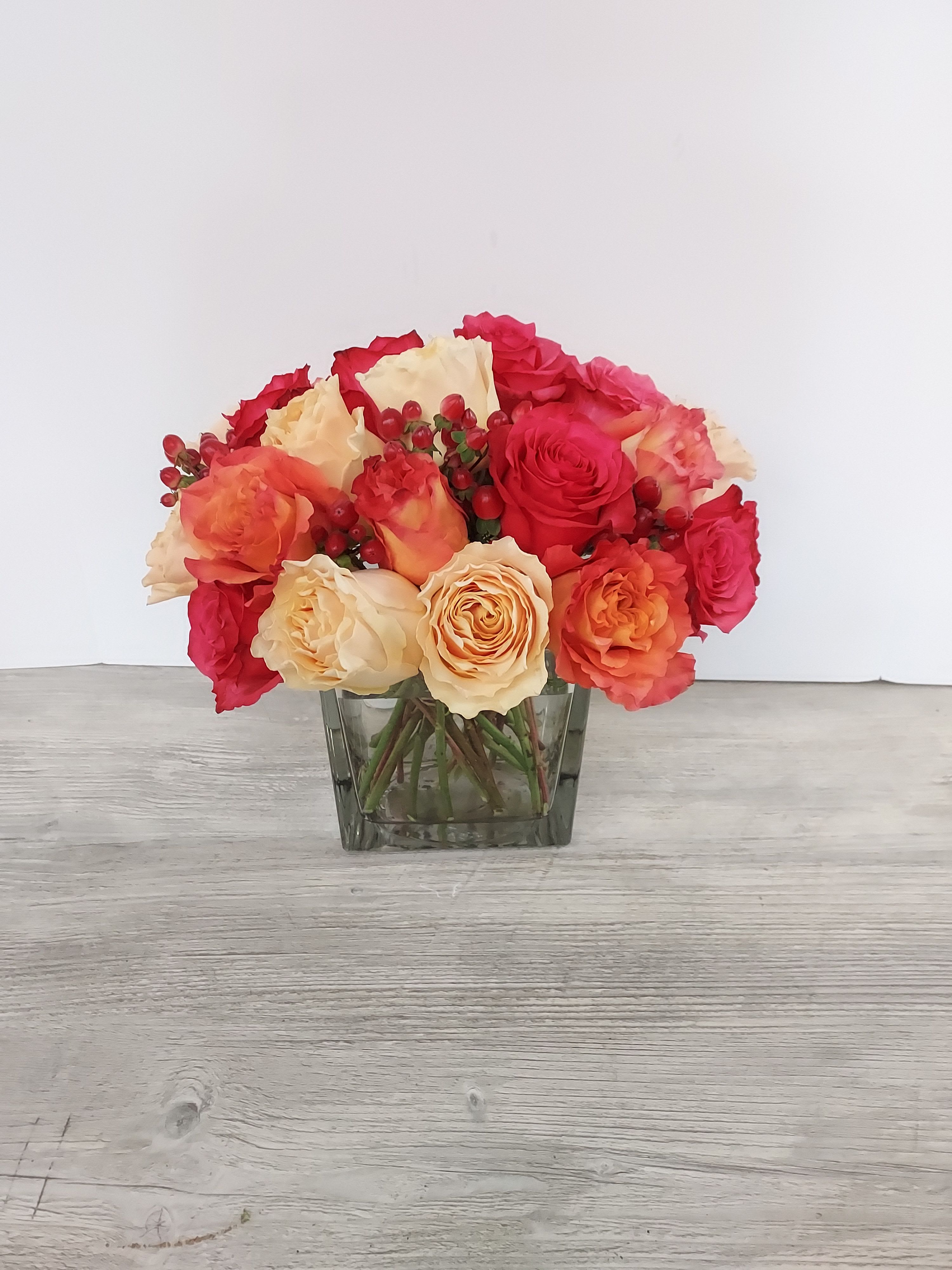 Low arrangement of red and peach roses with red berries in a clear glass cube vase