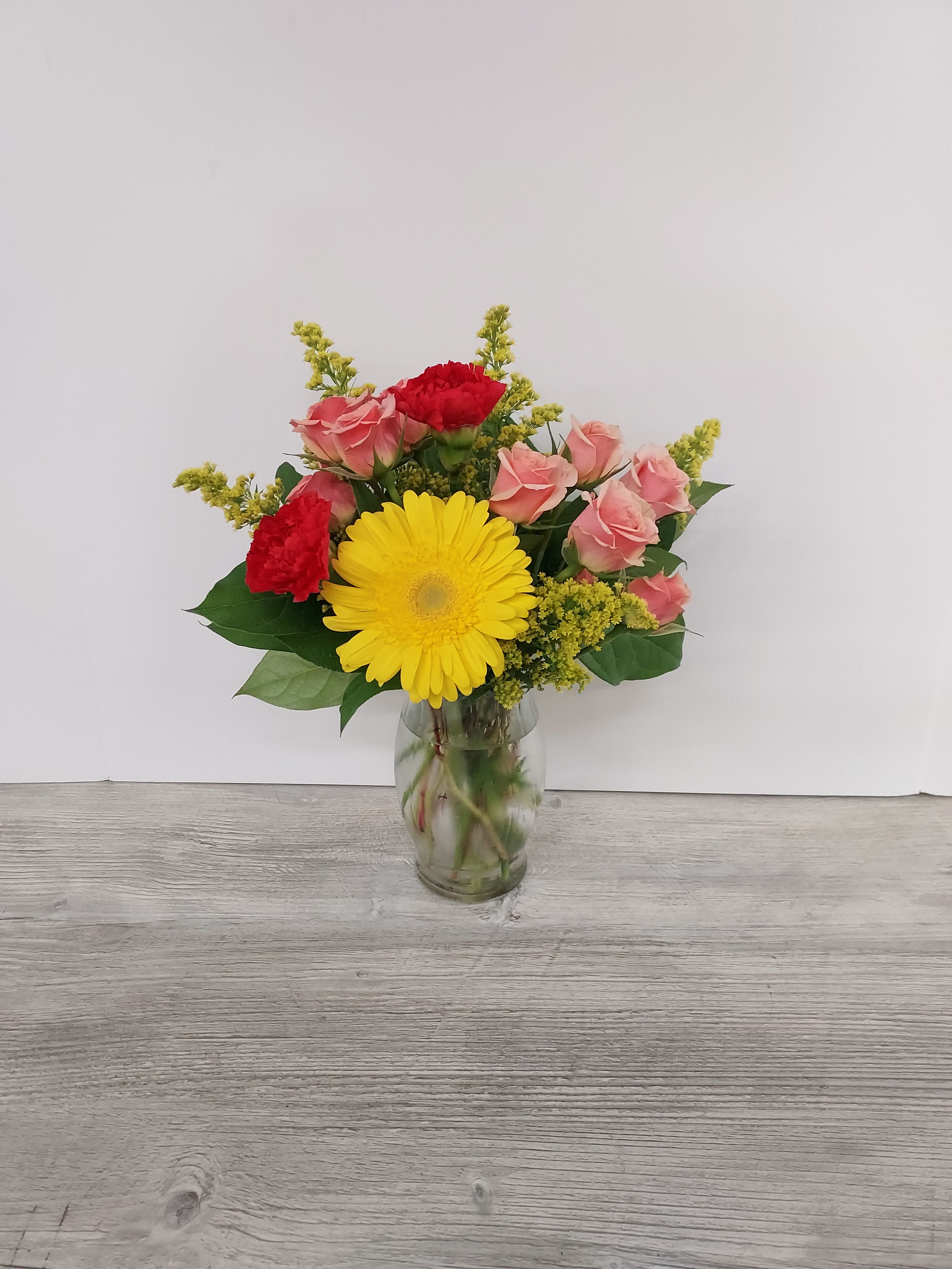 Small vase arrangement with yellow gerbera daisy, pink roses, and red carnations in a glass vase