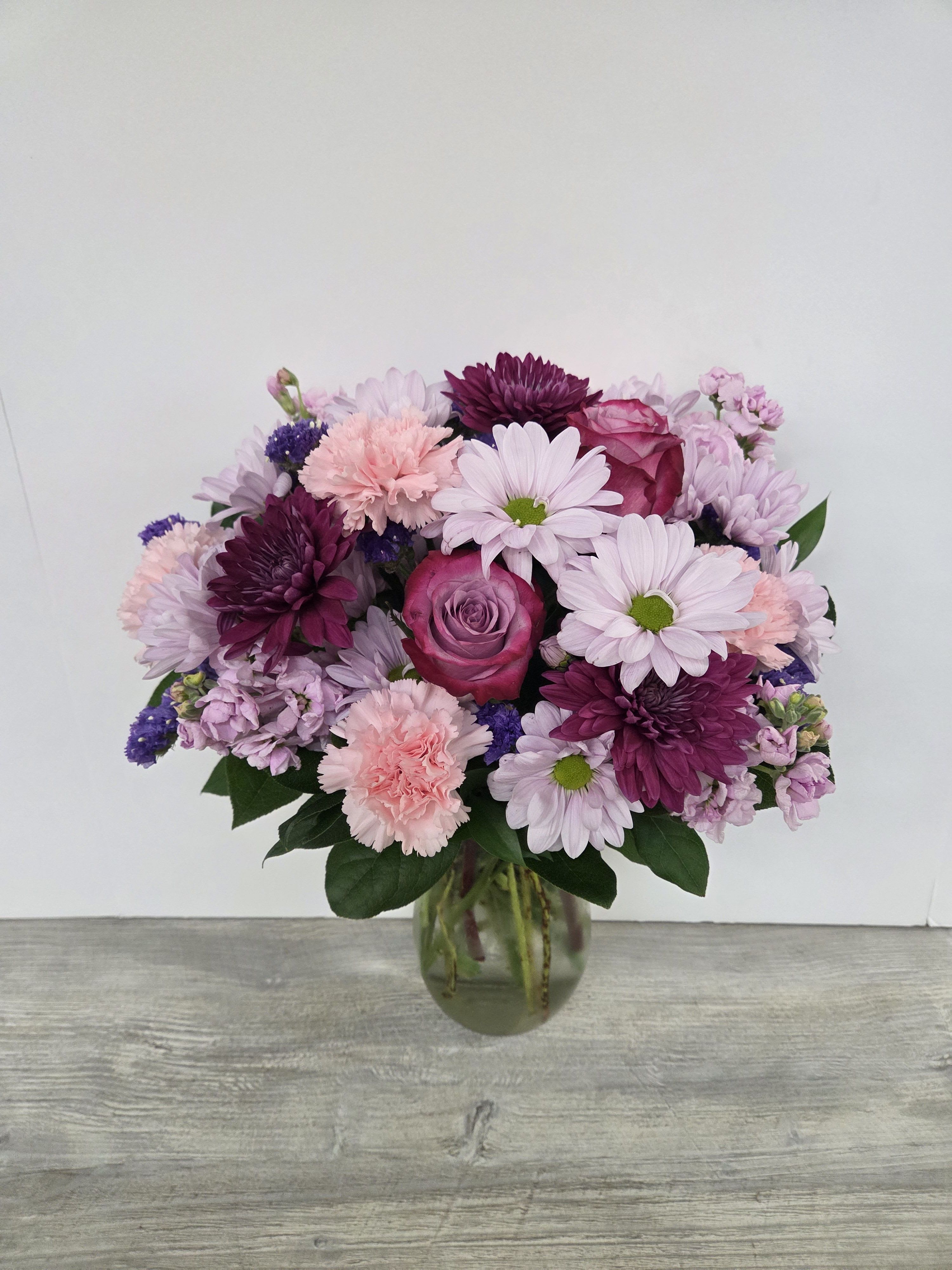 Vase of pink and purple roses, carnations, and daisies arranged in a rounded bouquet