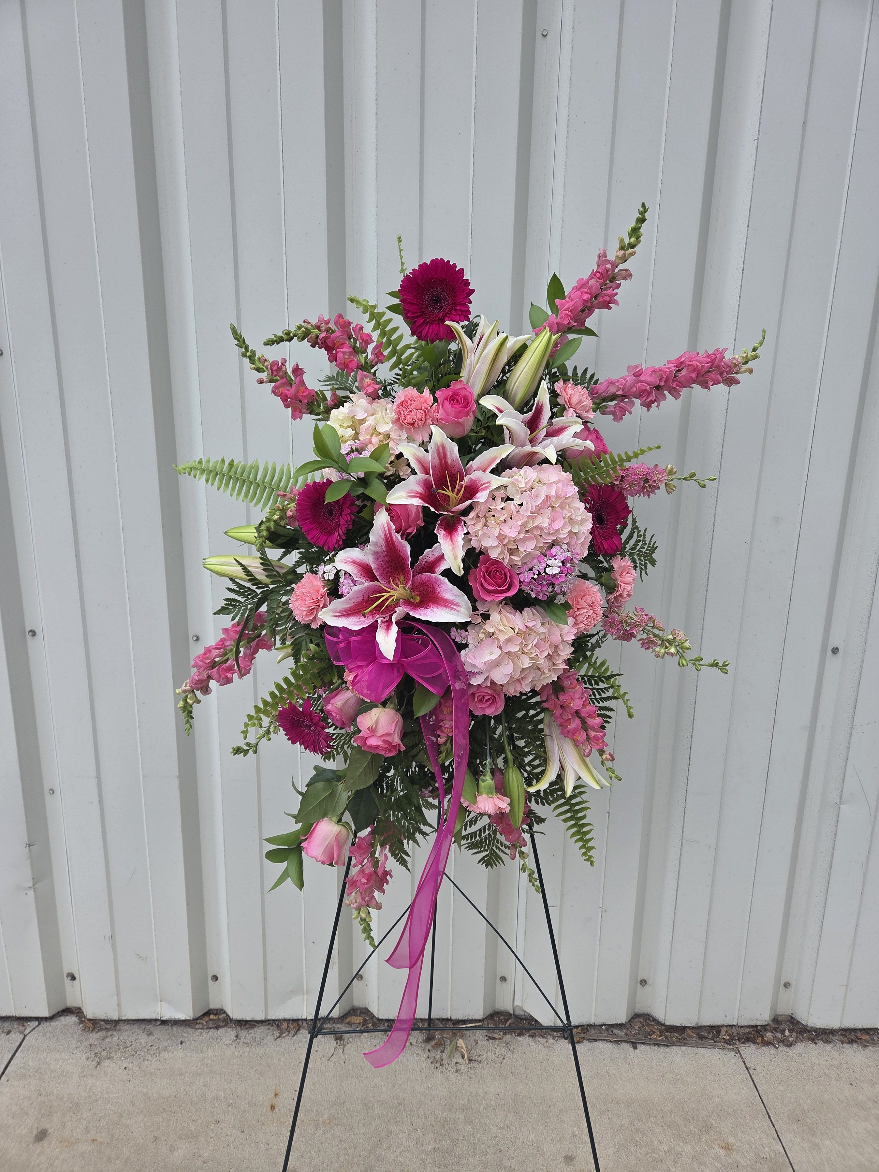 Standing spray of pink lilies, roses, carnations, gerbera daisies, and hydrangeas on a metal easel