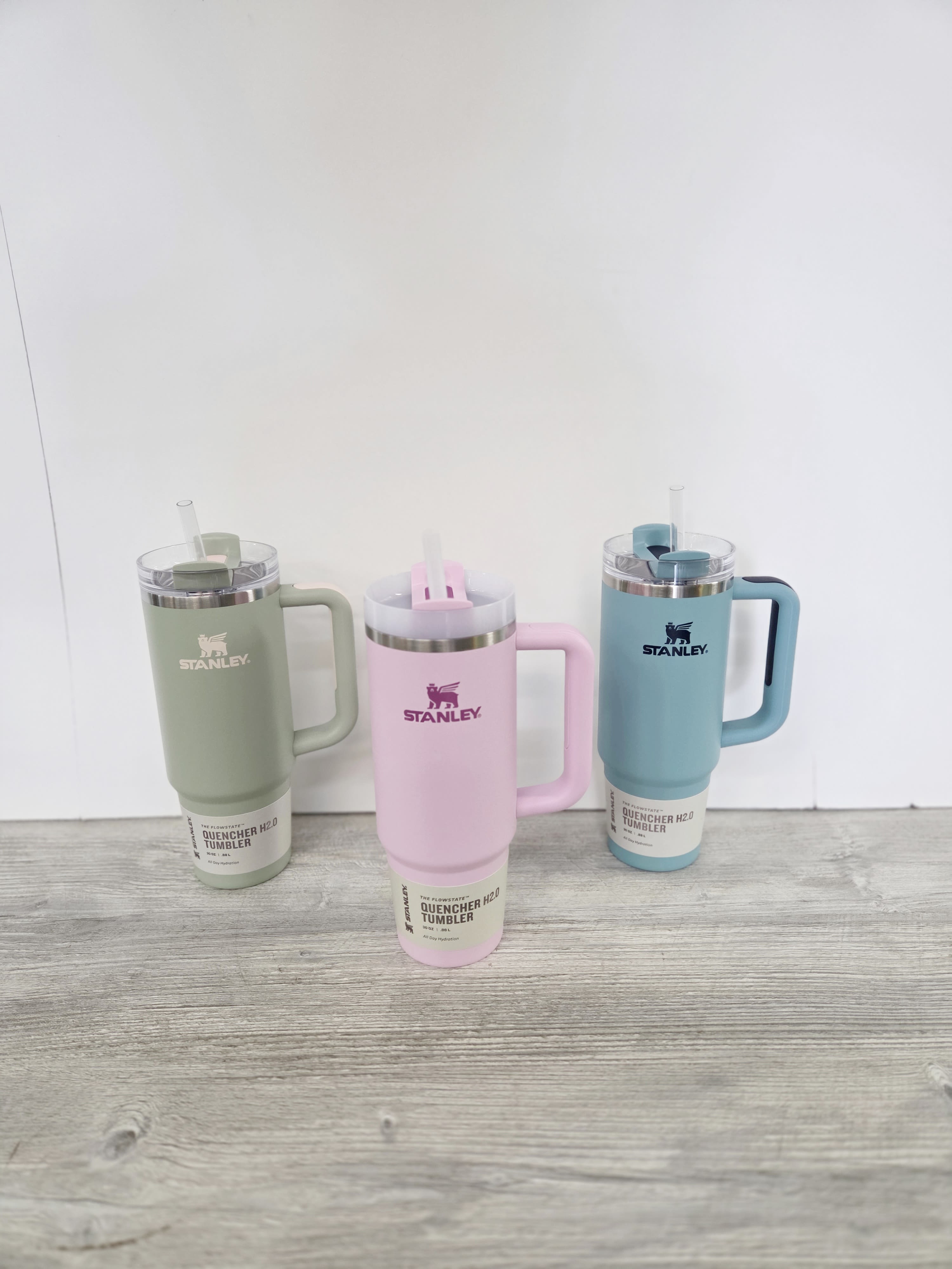 Set of three pastel Stanley handled tumblers with straws in green, pink, and blue on a wood surface