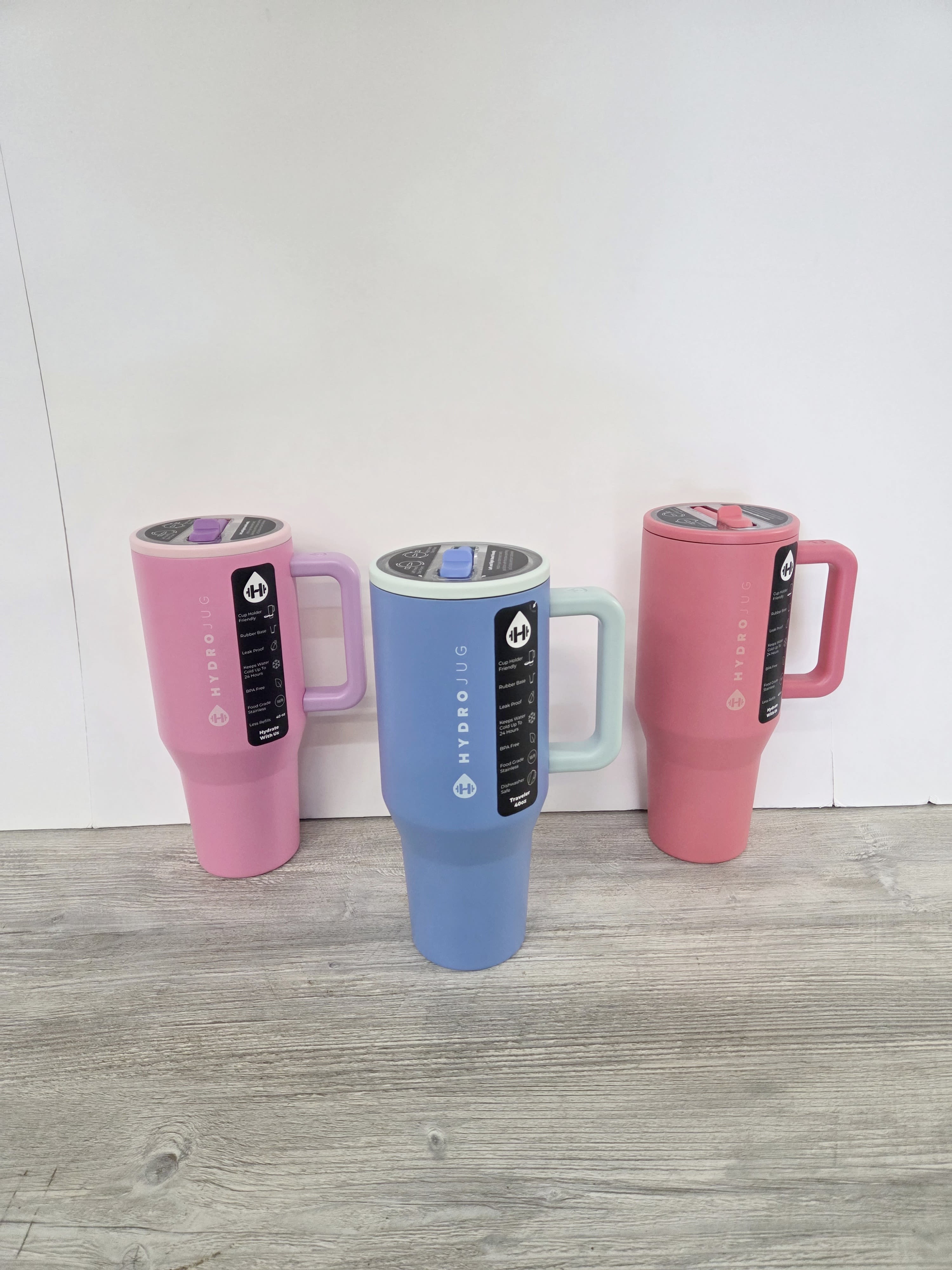 Set of three tall handled travel tumblers in pastel pink, blue, and coral on a wood floor