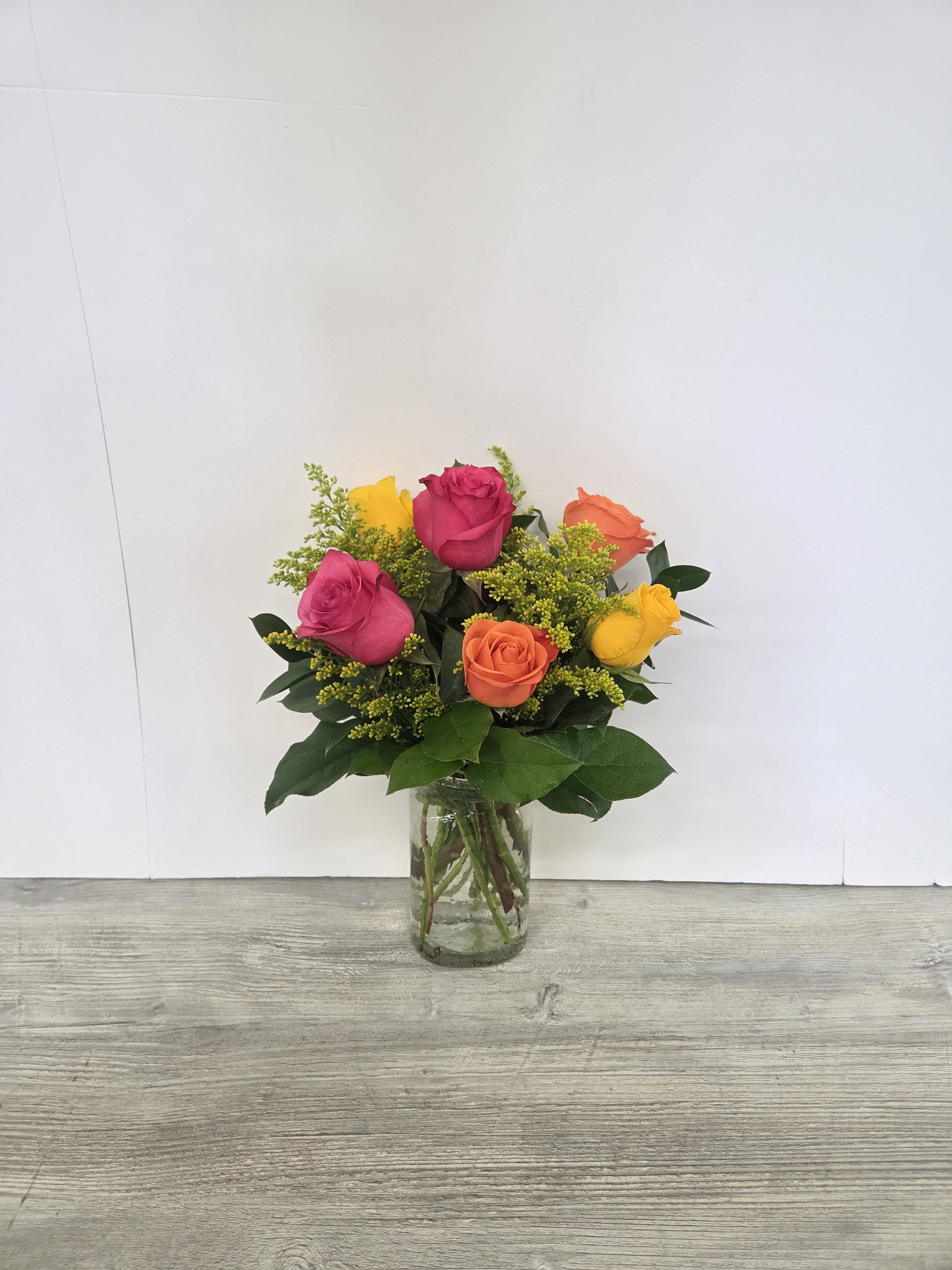 Bright bouquet of pink, yellow, and orange roses with yellow filler in a clear glass vase