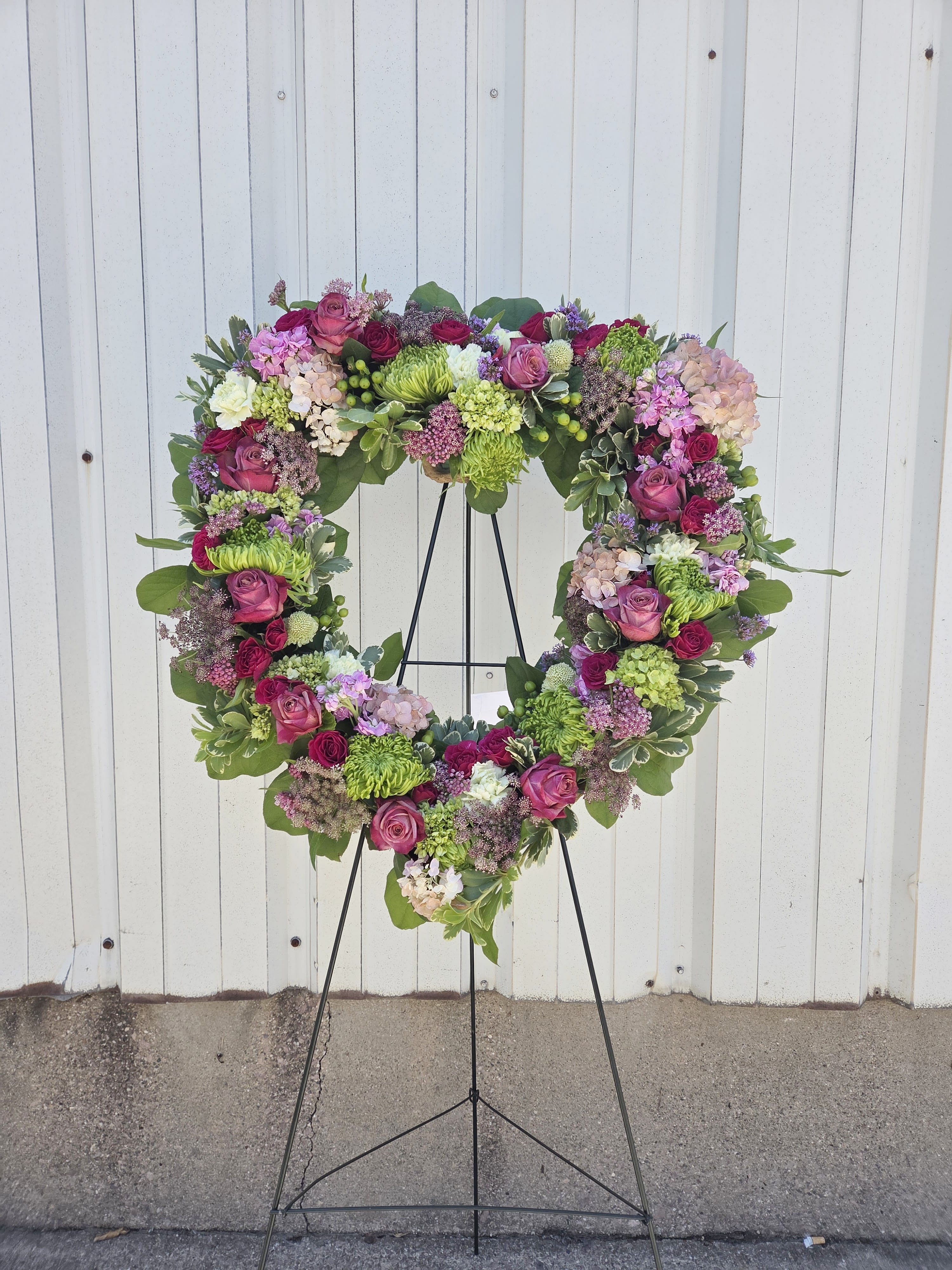 Heart-shaped standing wreath with pink roses, hydrangeas, and green mums on a metal easel