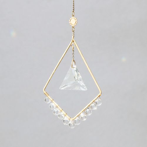 Geometric gold hanging ornament with clear crystal prism and beads on a gray background