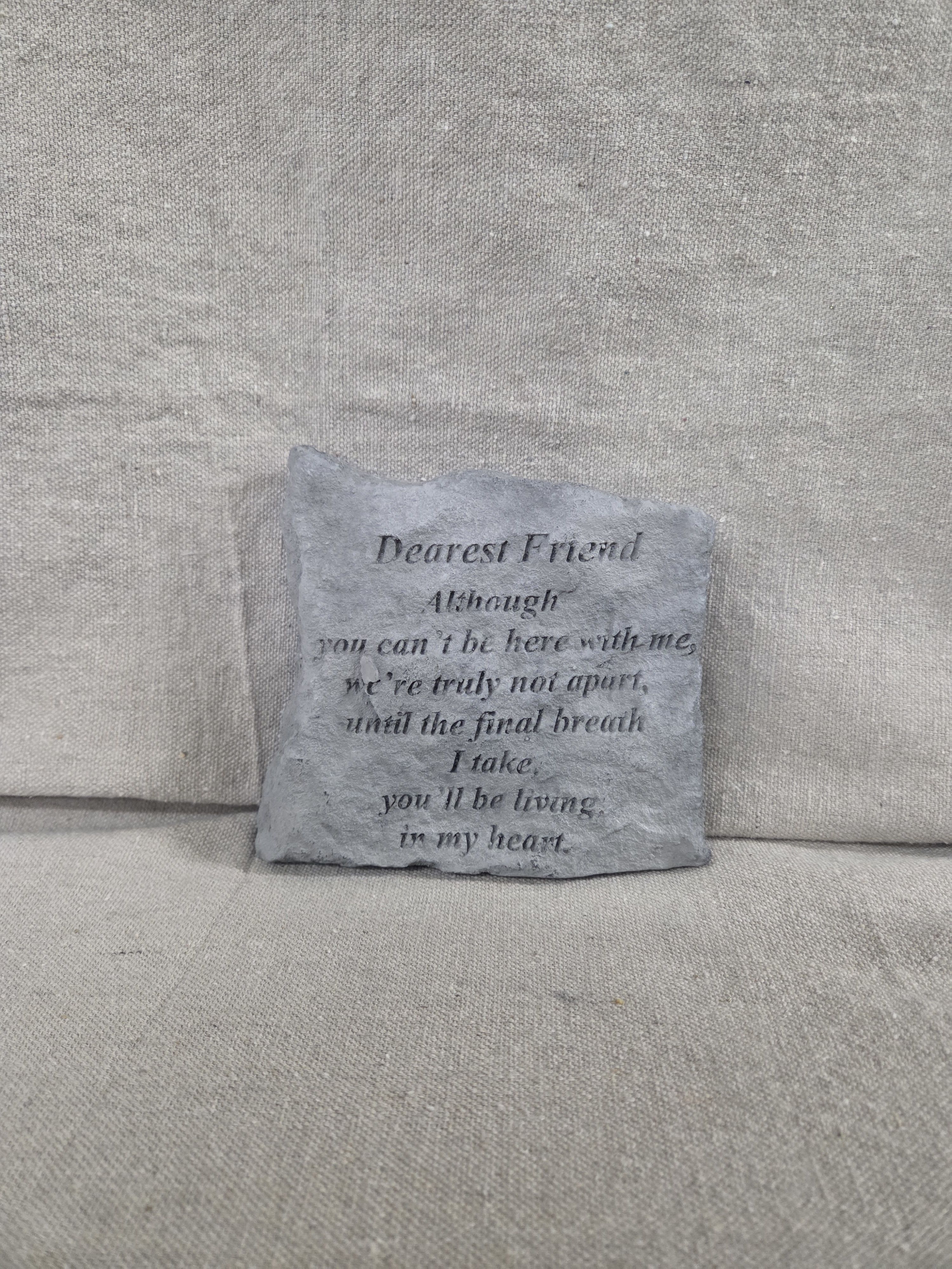 Square gray memorial stone with engraved poem text on a neutral fabric background